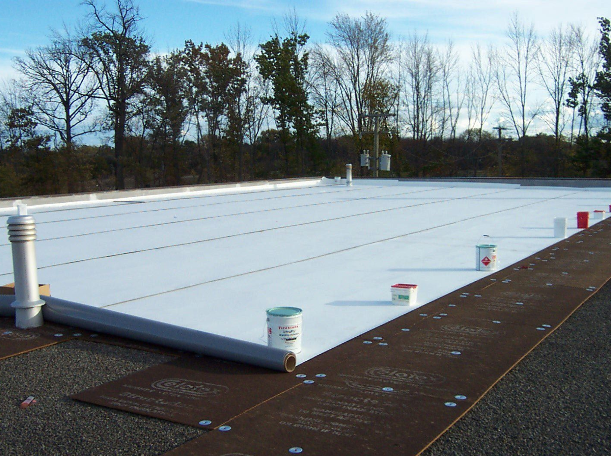 Industrial roof with a roll of white roofing material being installed.