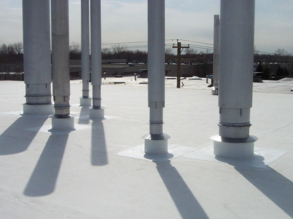 Gray commercial roofing on an assembly line plant, featuring a group of metal ventilation pipes on the roof.