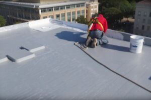 A contractor replacing an industrial roof, working with a bucket on the roof.