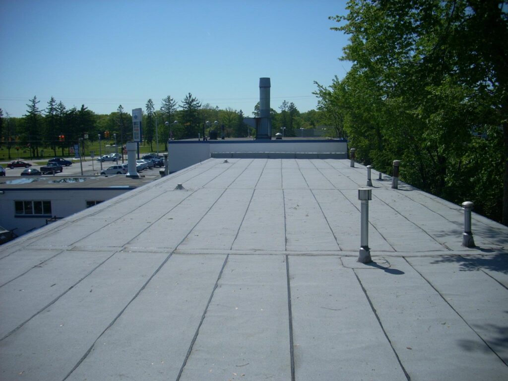 Gray commercial roofing on office building with ventilation pipes.