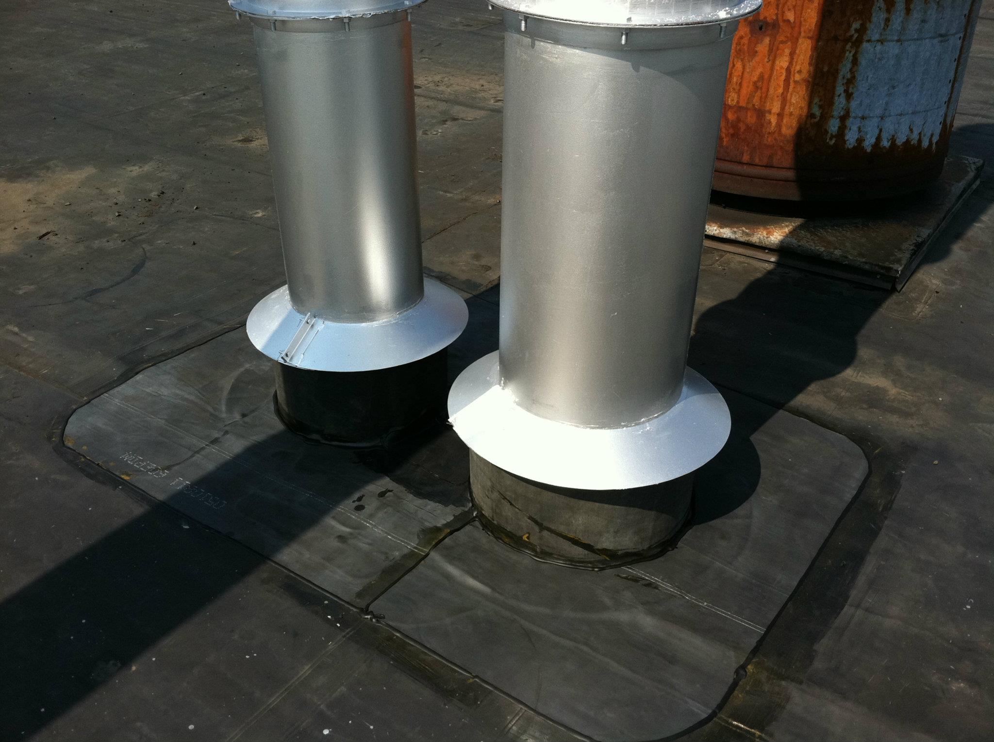 Two metal pipes on a roof with black commercial roofing material and waterproof sealant.